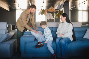 Modern bir mobilya galerisinde kanepe ve yastıkları karşılaştıran aile, evleri için rahat mobilyalar seçiyor.