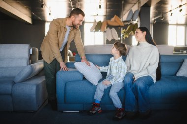 Ebeveynler ve oğulları modern bir mobilya dükkanında kanepe almak için alışveriş yapıyorlar. Daireleri için yeni parçalar seçiyorlar.