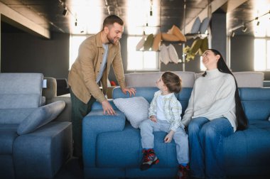 Modern bir mobilya galerisinde mutlu bir aile, anne ve oğlu bir kanepede otururken baba onların yanında duruyor.
