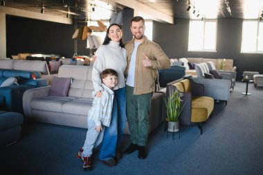 Genç ebeveynler ve çocukları bir arada duruyorlar. Evleri için neşeyle yeni bir kanepe seçiyorlar.