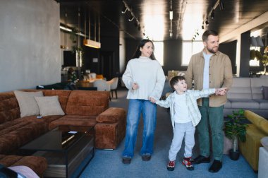 Ebeveynler ve küçük çocuklar el ele tutuşuyor, yeni ev dekorları için modern mobilya galerisini geziyorlar.