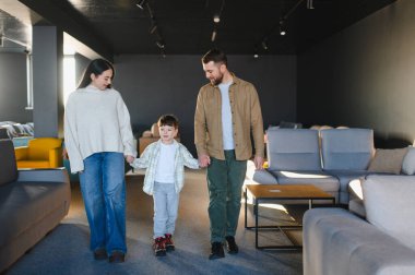 El ele tutuşan, mobilya galerisinde yürüyen, yeni kanepe ve dekorasyon ürünleri seçen mutlu aile.