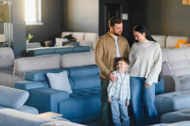 Genç bir aile, aileler ve çocuklar, mobilya galerisinde bir arada duruyorlar, evleri için yeni kanepeler bakıyorlar.