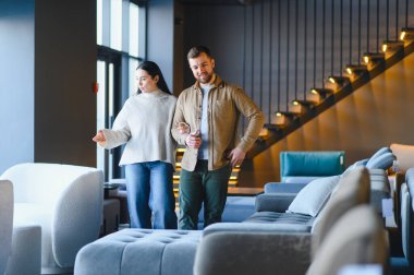 Çağdaş bir mobilya galerisinde farklı kanepeleri keşfeden genç bir çift, yeni daireleri için ev dekorasyonu seçiyorlar.