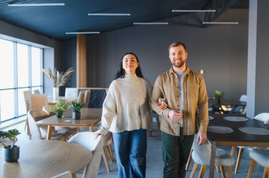 Gülümseyen çift yan yana duruyor, boş bir galeride modern mobilyalara bakıyor, ev dekorları için seçimler yapıyorlar.