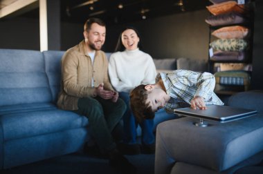 Mutlu bir ailenin mobilya dükkanını keşfetmesi, küçük oğulları kanepede oynarken ebeveynlerin gülümsemesi.