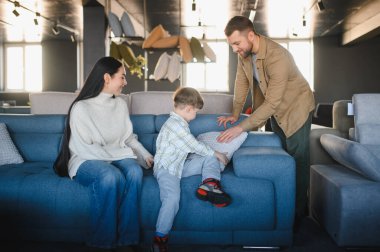 Ebeveynler ve küçük oğulları mobilya galerisindeki mavi kanepeyi inceliyor, yeni ev dekorasyonu seçiyor ve birlikte güzel vakit geçiriyorlar.