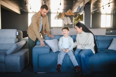 Mutlu aile, ebeveynler ve çocuklar, mobilya galerisindeki mavi bir koltukta oturuyor, gülümsüyor ve evleri için yeni mobilyalar seçerken eğleniyorlar.
