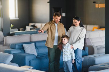 Aile üçlüsü mobilya mağazasında eğleniyor, ev için yeni bir kanepe seçiyor, birlikte önemli bir aile kararı veriyorlar.
