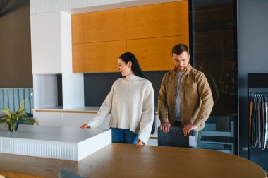 Modern mutfak tasarım seçeneklerini araştıran, dolapları seçen ve mobilya mağazasında ev yenilemesini tartışan genç bir çift.