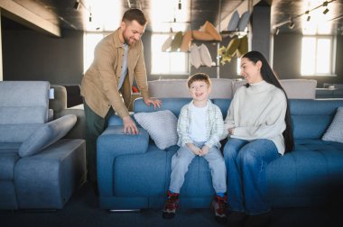 Ebeveynler ve oğulları mavi bir kanepede oturuyor, evleri için mobilya seçeneklerini araştırıyor, birlikte gülüyor ve gülüyorlar.