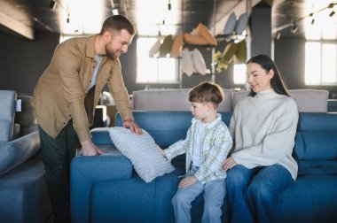 Genç bir aile, ebeveynler ve çocuk, mobilya mağazasından kanepe alıyorlar. Evleri için seçenekler arıyorlar.