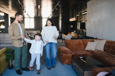 Mutlu bir aile, çocuklu bir çift mobilya mağazasında yürüyor, kanepeleri ve dekorları keşfediyor.