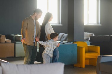 Mobilya galerisini keşfeden genç bir aile, yeni ev eşyaları ararken ebeveynler çocuklarının elini tutuyor.
