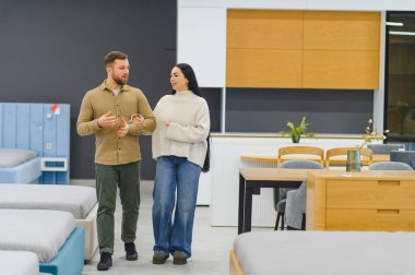 Çağdaş bir mobilya mağazasında yürüyen ve tartışan genç çift, ev dekorasyonu ve iç tasarım çözümleri arıyor