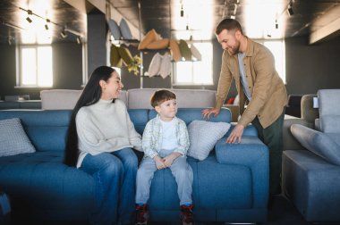 Genç bir aile evi için yeni bir kanepe seçiyor, mutlu ebeveynler mobilyaları ev dekorasyonu için karıştırıyor.