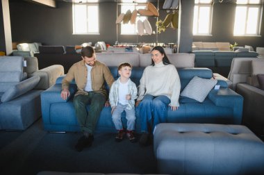 Happy ailesi modern bir mobilya mağazasında mavi kanepeyi test ediyor ve yeni ev dekorasyonu unsurlarını seçiyor.
