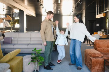 Ebeveynler mutlu bir çocuğu kaldırıyor, geniş bir mobilya galerisinde oynuyor ve gülümsüyor, aile birlikteliğini ve boş zamanlarını yaşıyor.