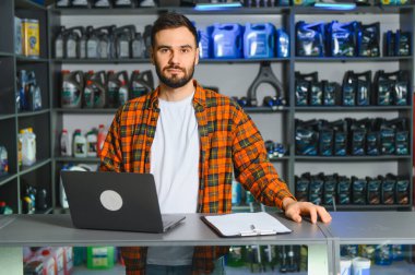 Tezgahın arkasında dizüstü bilgisayar yöneten ve profesyonel bir otomotiv parçası dükkanında sipariş veren adam kendinden emin ve ciddi görünüyor.
