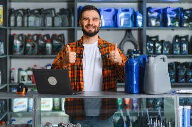 Araba yedek parça mağazasında gülümseyen bir işçi mükemmel müşteri hizmetleri sunuyor. Arkaplanda araba bakım ürünleriyle dolu raflar
