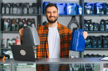 Araba parçacıda çalışan gülümseyen adam müşterilere motor yağı şişelerini sunuyor. Otomotiv hizmeti ve bakım kavramı