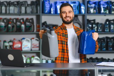 Otomotiv tezgahında çalışan gülümseyen adam müşteri seçimi için farklı motor yağları sunuyor.