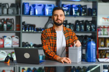 Araba aküsü ve motor yağıyla tezgahın arkasında duran gülümseyen bir satıcı.