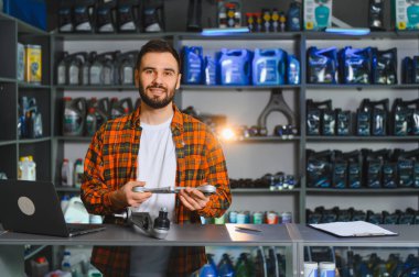 Otomobil yedek parça mağazasında çalışırken kameraya gülümseyen bir adam, İngiliz anahtarı tutuyor ve ürünler sunuyor