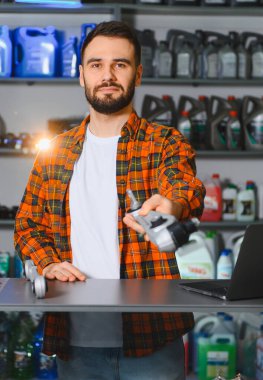 Erkek otomotiv teknisyeni araba parçası tutuyor, bir otomobil mağazasında dizüstü bilgisayarla duruyor.