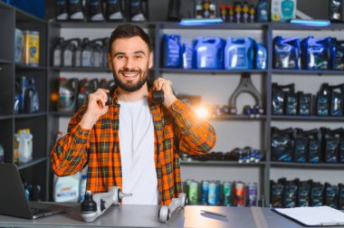 Gülümseyen adam bir otomobil parçası mağazasında sunum yapıyor, mekanik aletler tutuyor ve araba süspansiyon parçalarını gösteriyor