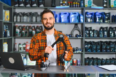 Bir oto yedek parça mağazasında çalışan gülümseyen adam, araç süspansiyonu için kontrol kolu ve topçu eklemi tutuyor.