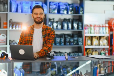 Otomobil parçaları reyonunda sakallı mağaza asistanı yoğun perakende satış, envanter ve müşteri hizmetlerini yönetmek için dizüstü bilgisayar kullanıyor.