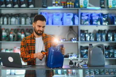 Adam motor yağı şişesini barkod tarayıcısıyla kaydederken aynı zamanda otomobil parçaları deposuna ürün verilerini giriyor