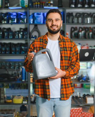 Araç bakım ürünleri için alışveriş yapan bir adam, perakende mağazasında gri bir motor yağı kutusu tutuyor.