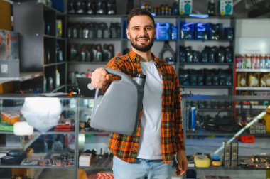 Gülümseyen, elinde motor yağı kabı olan bir adam, araba bakımı için araç yağlarını bir perakendeciden seçen bir adam.
