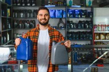 Araba yağı almak için alışveriş yapan bir adam, bir otomotiv dükkanında iki kutu motor yağı tutuyor. Otomotiv bakım kavramı