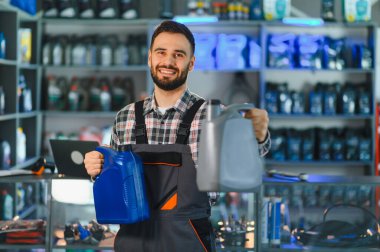 Ekose gömlekli ve tulumlu gülümseyen servis elemanı araba bakımı ve müşteri desteği için motor yağı şişesi sunuyor.