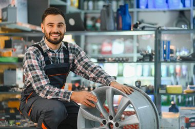 Otomobil tamirhanesinde çalışan gülümseyen tamirci, bir alaşım tekerleği tutuyor, otomotiv tamiri ve bakımı sağlıyor.