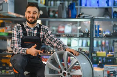 Otomotiv işçisi parlak bir araba kenarına çömelmiş, bir garajda veya parça dükkanında yeni bir yedek parça sunuyor