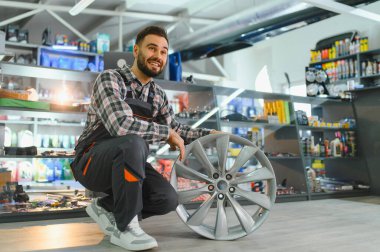 Gülümseyen adam araba tamirhanesinde bir araç kenarı sunuyor, otomotiv ve bakım sektöründe çalışıyor.