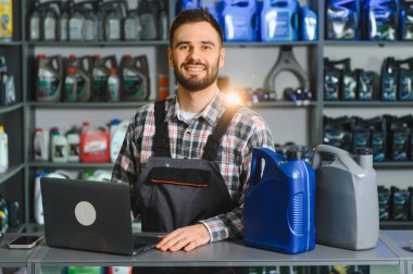 Tezgahta duran tamirci, motor yağı kutularıyla dizüstü bilgisayarda çalışıyor, envanter ve müşteri hizmetlerini yönetiyor.