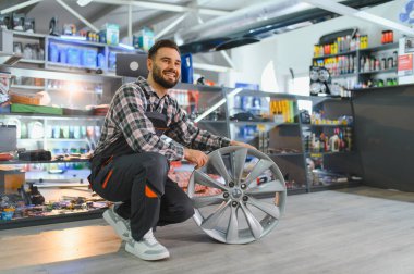 Gülümseyen tamirci, şık bir alaşımlı araba tekerleği tutuyor, bir otomotiv mağazasında hizmet ve uzmanlık sunuyor.