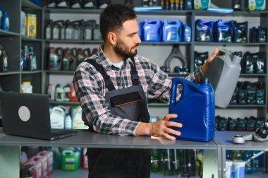 Tamirci araba bakımı için farklı kayganlaştırıcıları karşılaştırıyor, bir otomotiv tamirhanesinde tezgahın yanında duruyor.