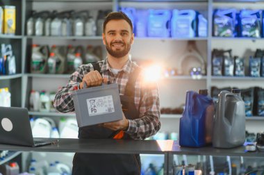 Gülümseyen tamirci yeni bir araba aküsünü sunuyor, bir otomotiv dükkanında müşterilere hizmet ve uzmanlık sağlıyor