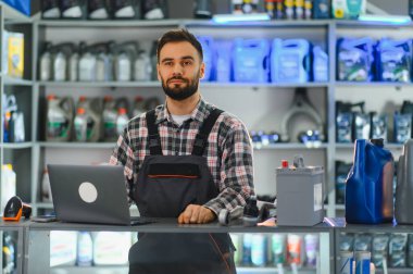 Tezgahta dizüstü bilgisayar ve araba parçalarıyla duran atölye çalışanı, özel perakende mağazasında hizmet sunuyor