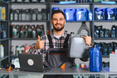 Motor yağı konteynırını tutan tamirci ya da tezgahtar, otomotiv parçaları dükkanında dizüstü bilgisayarla işaret veriyor.