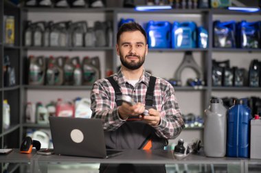 Tamirci, yeni araba parçası sunuyor. Bir tamirhanede dizüstü bilgisayar ve motor yağı ekranıyla çalışıyor.