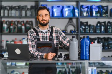 Servis merkezi danışmanı dizüstü bilgisayar ve araba parçaları ile ayakta duruyor, araç mağazasında yardım ve envanter yönetimi sağlıyor