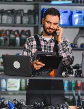 Oto tamircisi atölyede akıllı telefondan pano ve dizüstü bilgisayarla konuşuyor. Profesyonel teknisyen emir ve parçaları yönetir.