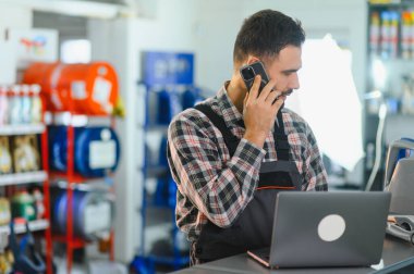 Otomobil servisi çalışanı çevrimiçi siparişleri işliyor ve atölyedeki cep telefonundan müşteri sorularını cevaplıyor